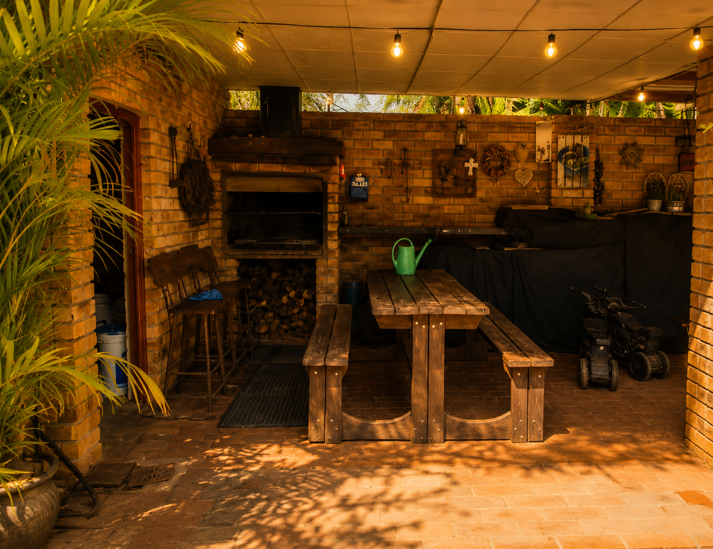 Covered braai area with wooden picnic table and warm hanging lights at Protea Guesthouse
